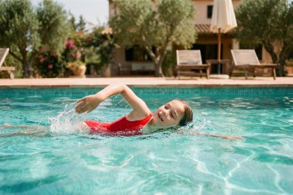 Jeune fille apprenant à nager seule dans une piscine extérieure lors de vacances en famille en été