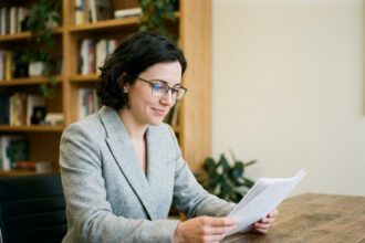 Femme portant des lunettes à verres antireflet en train de lire des documents dans un bureau moderne, illustrant le confort visuel offert par le traitement antireflet