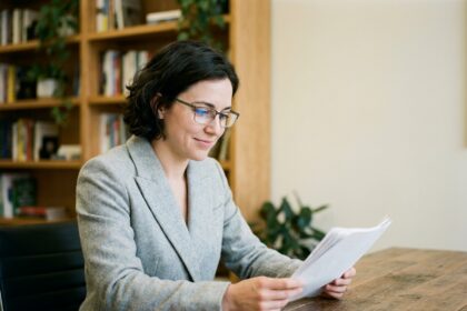 Femme portant des lunettes à verres antireflet en train de lire des documents dans un bureau moderne, illustrant le confort visuel offert par le traitement antireflet